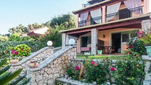 A two-story house with a stone staircase, a balcony with a checkered tablecloth, and a garden with flowers. - 'Villa Pepy Luxury Apartment' with Mountain View, Garden & Wi-Fi (Corfu)