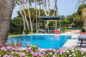 Una piscina con lettini, una pergola e vegetazione circostante.