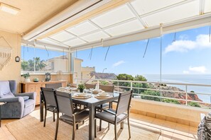 A dining area with a table set for four, a sofa, and a view of the sea. - Penthouse 'Acag 096' in Front of the Sea View, Wi-Fi & A/C (Dehesa de Campoamor)