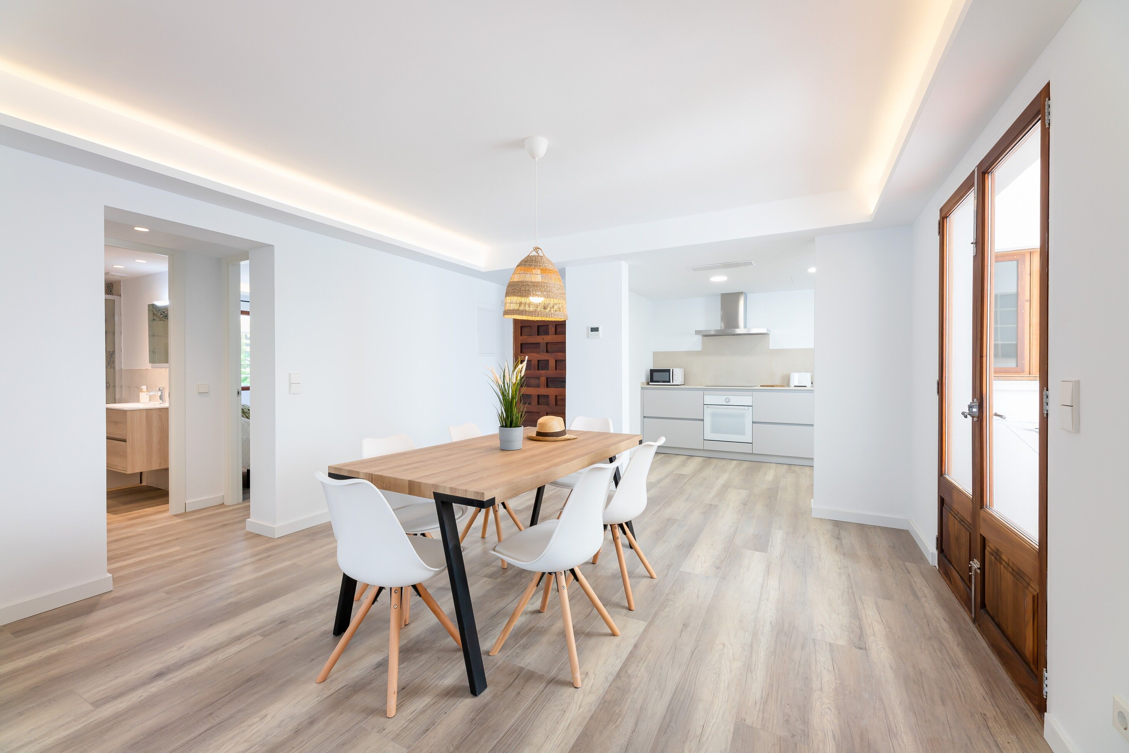Un espace de salle à manger moderne avec une table en bois, des chaises blanches et un luminaire suspendu.