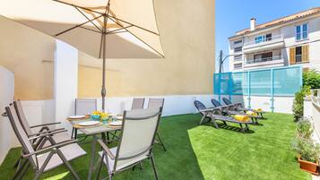 Une terrasse extérieure avec une table et des chaises, un parasol suspendu et un bâtiment en arrière-plan.