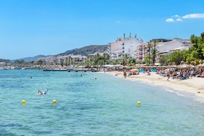 Une plage avec une eau claire, des parasols et des gens.