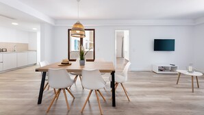 A modern kitchen with white cabinets, a dining table with chairs, a hanging light fixture, and a flat-screen TV mounted on the wall. - Apartment 'Albercutx Pollentia 2' with Wi-Fi and Air Conditioning (Puerto Pollensa)