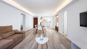A modern living room with a sofa, a dining table with chairs, a kitchen in the background, and a TV mounted on the wall. - Apartment 'Albercutx Pollentia 2' with Wi-Fi and Air Conditioning (Puerto Pollensa)