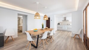 A modern dining area with a wooden table, white chairs, pendant lights, and a kitchen in the background. - Holiday Apartment 'Albercutx Pollentia 3' Near the Beach with Private Terrace (Pollensa)