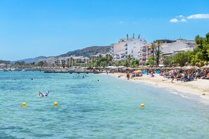 A beach with clear water, umbrellas, and people.