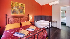 A bedroom with a bed, a bathtub, a painting, and an air conditioning unit.