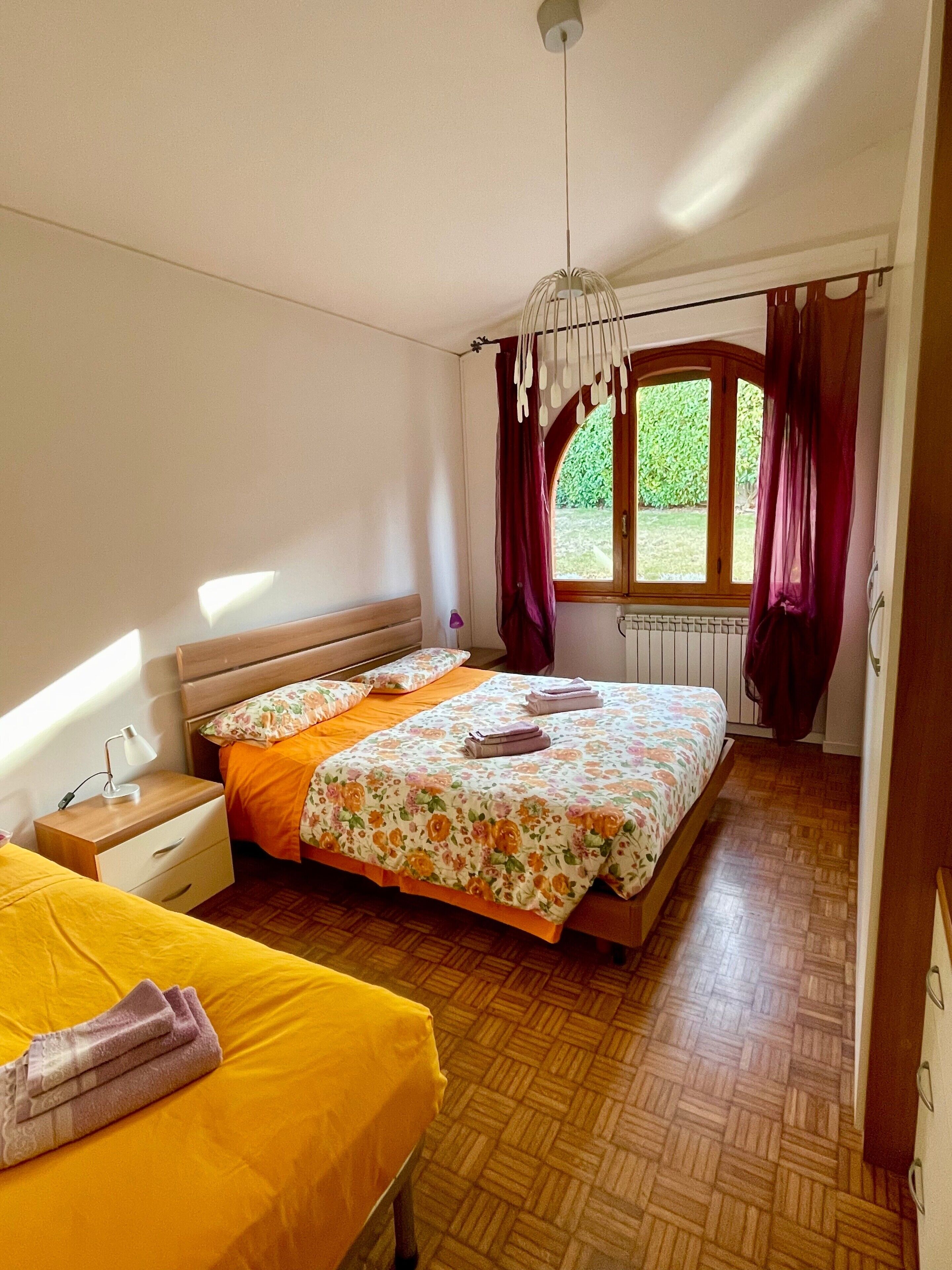 Une chambre à coucher avec un lit, une table de chevet, une fenêtre avec des rideaux et un radiateur.