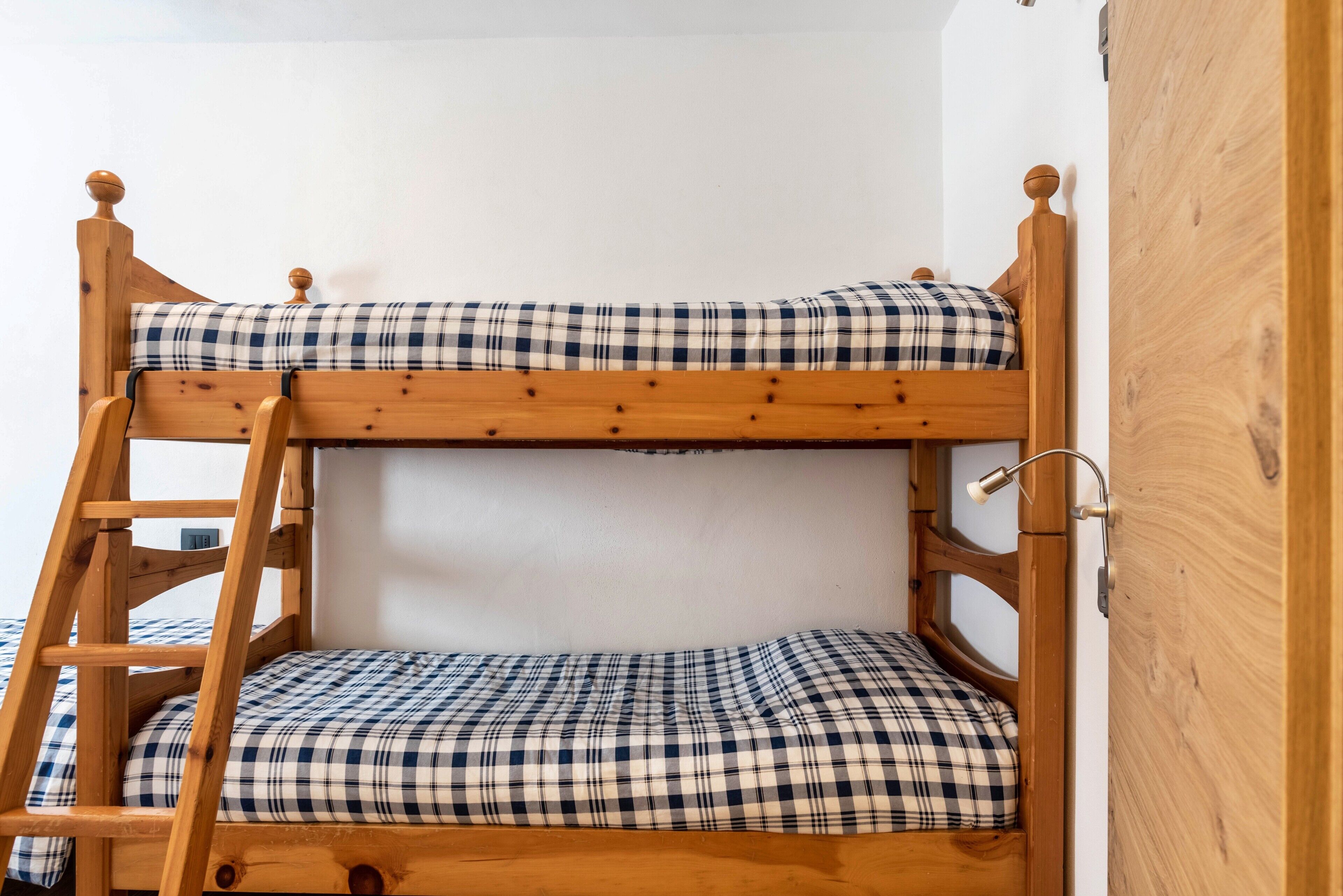 Un lit superposé avec une échelle en bois, une couverture à carreaux et une tête de lit en bois.