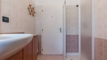 Un baño con un lavamanos blanco, armarios de madera, una puerta blanca y una zona de ducha con mampara de vidrio.