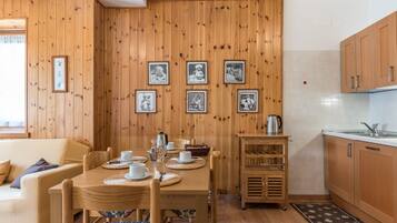 A wooden-paneled room with a dining table set for two, a kitchen area with wooden cabinets, and framed pictures on the wall.