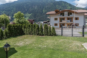 A two-story building with a tiled roof, surrounded by a well-maintained lawn and a row of evergreen trees.