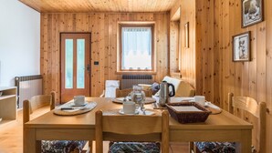 A wooden-paneled room with a dining table set for two, a window with curtains, and a radiator. - Appartamento Adamello Casa Lucia – Mountain View, Garden, Parking (Pinzolo)