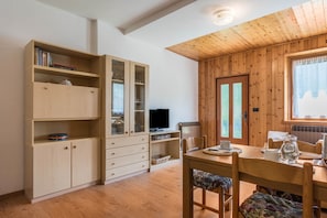 A wooden-paneled room with a dining table, chairs, a television, and built-in shelving.