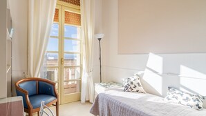 A hotel room with a bed, a chair, a nightstand, a lamp, and a window with curtains. - Apartment "Casa di Alice" with Sea View, Balcony and Wi-Fi (Siracusa)
