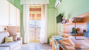 A room with a sofa, a glass-top table, a TV, a red clock, and a cactus. - Apartment "Casa di Alice" with Sea View, Balcony and Wi-Fi (Siracusa)