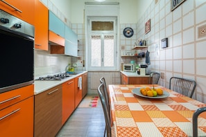 A compact kitchen with orange cabinets, a stove, a microwave, and a dining table with a fruit plate. - Apartment "Casa di Alice" with Sea View, Balcony and Wi-Fi (Siracusa)