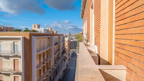 A narrow urban street with multi-story buildings, balconies, and a clear sky. - Apartment "Casa di Alice" with Sea View, Balcony and Wi-Fi (Siracusa)