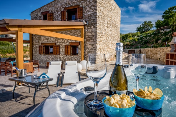 Un bâtiment en pierre avec une piscine, un espace extérieur aménagé et une bouteille de vin.
