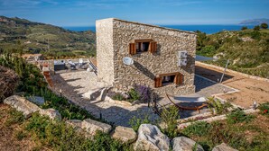 A stone building with a terrace, outdoor seating, and a view of the sea.