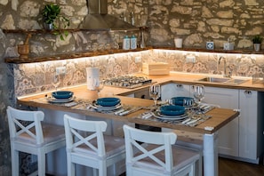 Une cuisine avec un mur en pierre, une cuisinière à gaz, un évier et des chaises blanches.