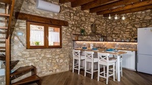 A kitchen with stone walls, wooden beams, a white refrigerator, and a bar area with white chairs.