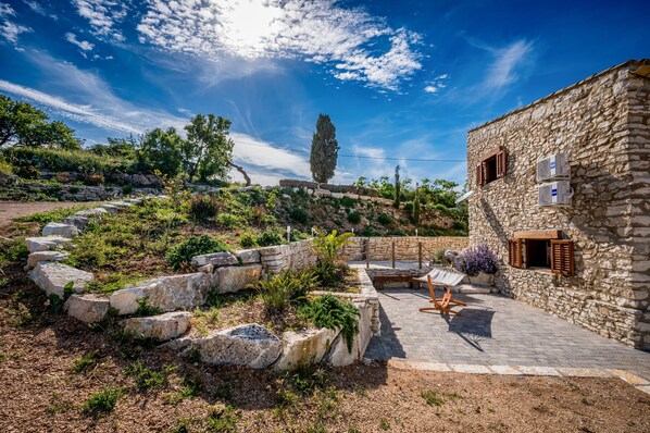 Un edificio de piedra con un patio empedrado, asientos exteriores y un muro de contención de piedra.