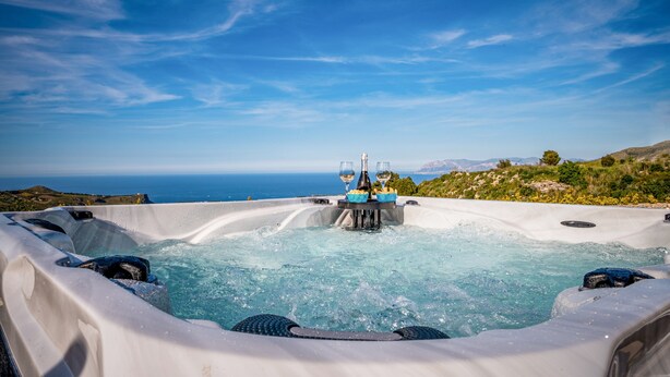A hot tub with a table and two glasses, overlooking a scenic ocean view.