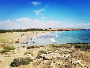 Une plage animée, un ciel dégagé et un premier plan rocheux.