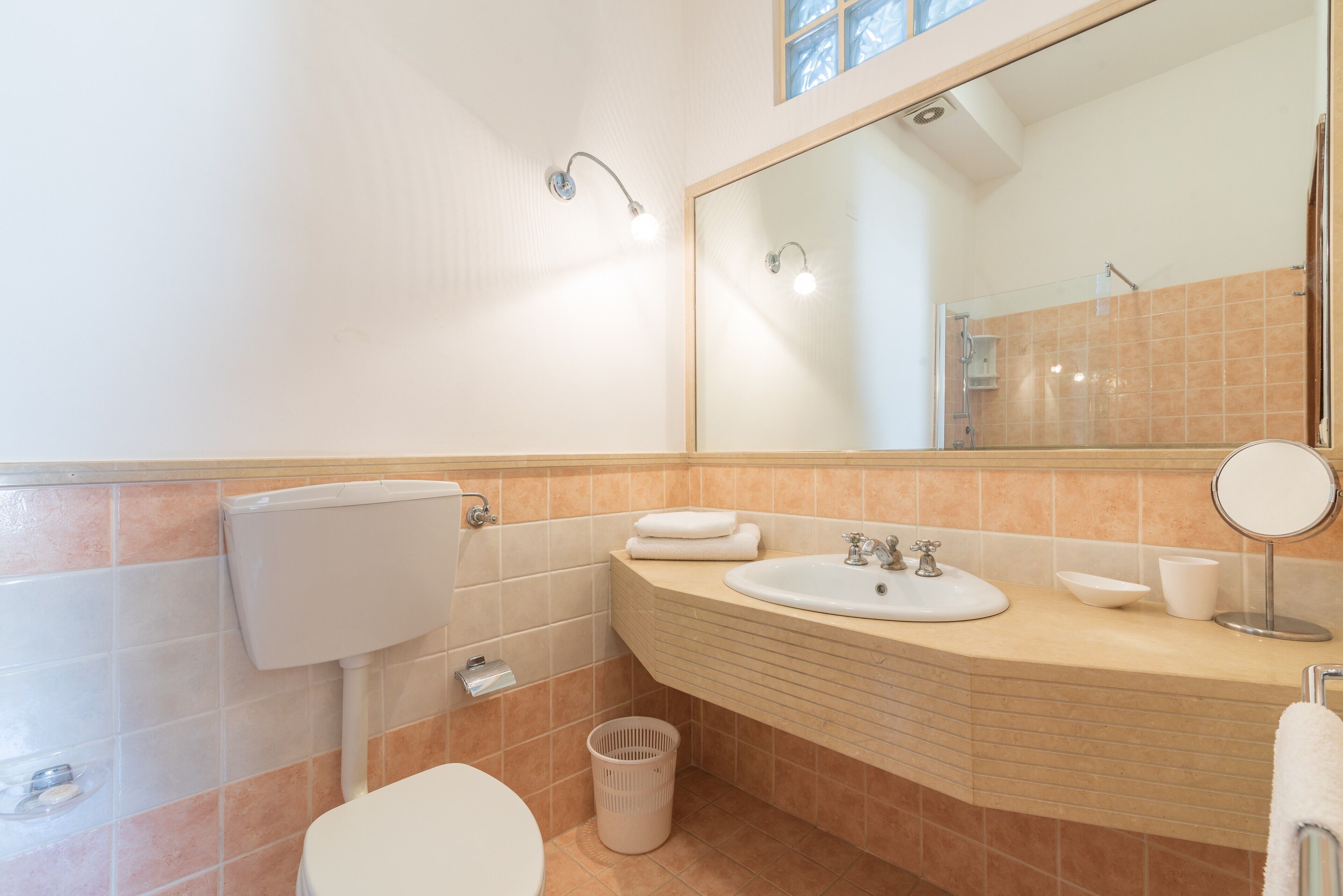 A bathroom with a toilet, sink, mirror, and a trash bin.
