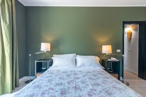A bed with a floral bedspread, two bedside lamps, a nightstand, and a door with a light fixture.