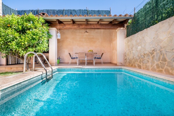 A swimming pool with a stone wall and a covered patio area with a table and chairs.