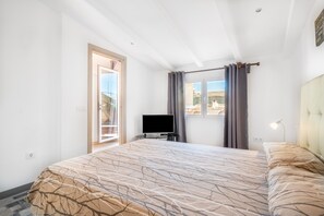 A bedroom with a bed, a television, a window with curtains, and a view of the outside.