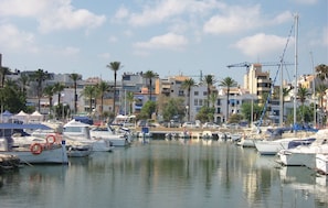 Un port de plaisance avec des bateaux amarrés, des bâtiments en arrière-plan et des palmiers.