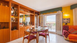 A living room with a glass-top dining table, wooden cabinets, and a sofa with a patterned throw. - Holiday Home 'Villa Lilia' with Sea View, Private Pool and Wi-Fi (Vilanova i la Geltrú)