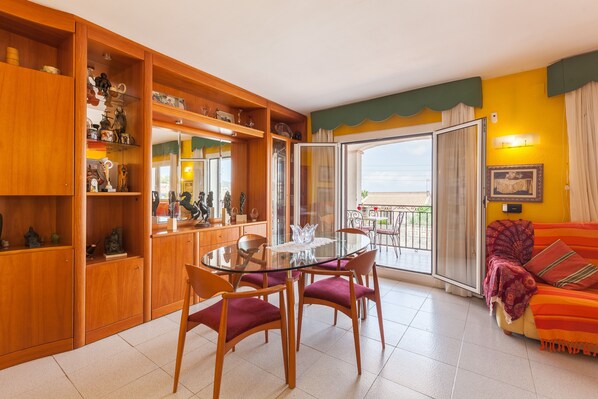 A living room with a glass-top dining table, wooden cabinets, and a sofa with a patterned throw.