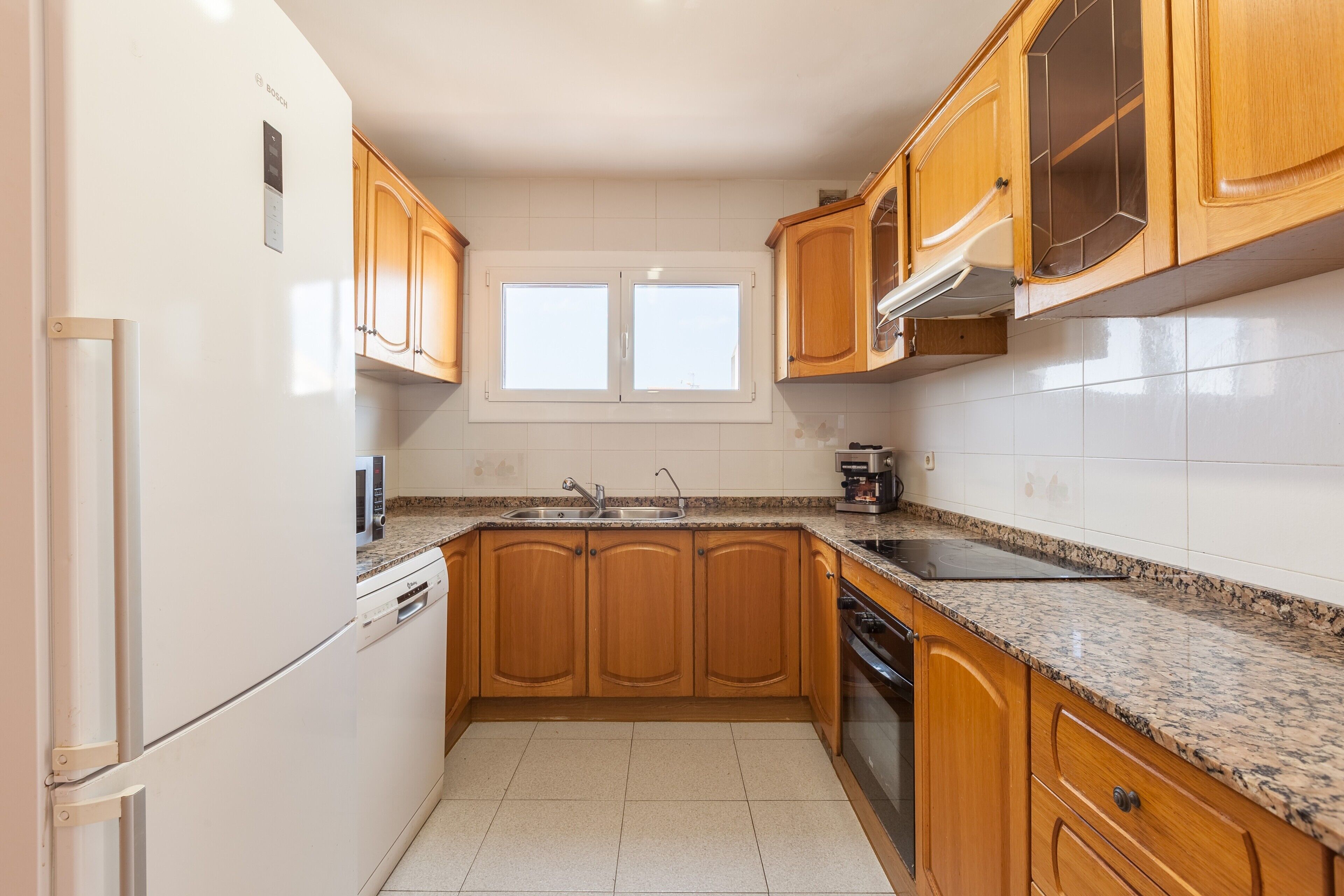 A kitchen with wooden cabinets, a built-in oven, a microwave, and a window above the sink.