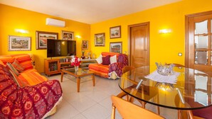 A living room with a sofa, television, and a glass table. - Holiday Home 'Villa Lilia' with Sea View, Private Pool and Wi-Fi (Vilanova i la Geltrú)