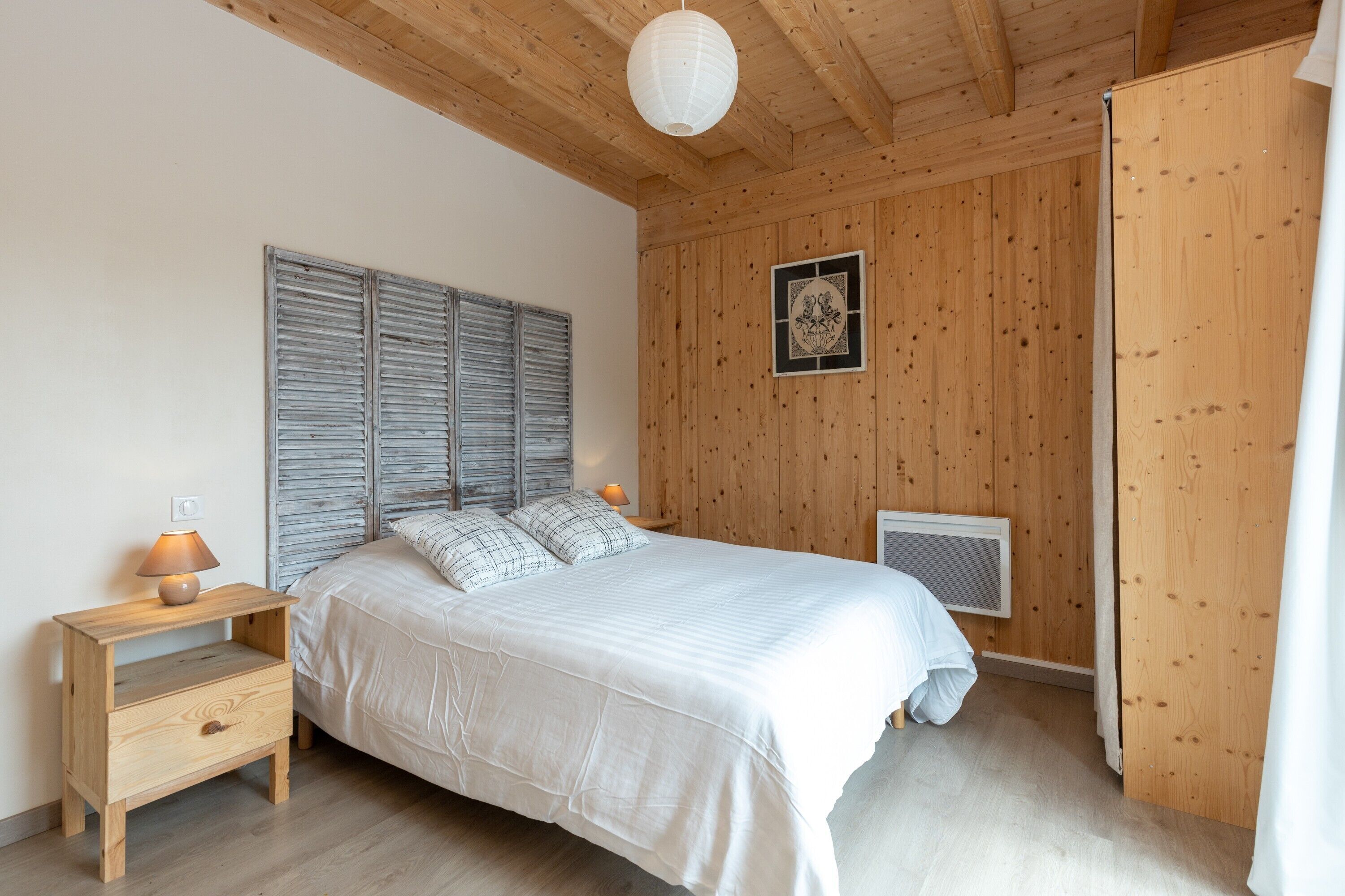 Ein Schlafzimmer mit Holzboden, einem Bett mit weißer Bettdecke, einem Nachttisch mit Lampe und einem gerahmten Bild an der Wand.