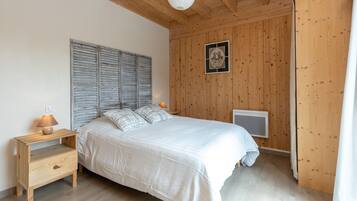 Ein Schlafzimmer mit Holzboden, einem Bett mit weißer Bettdecke, einem Nachttisch mit Lampe und einem gerahmten Bild an der Wand.
