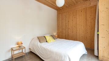 Een slaapkamer met een houten plafond, een bed met witte beddengoed, een nachtkastje met een lamp en een houten garderobe.