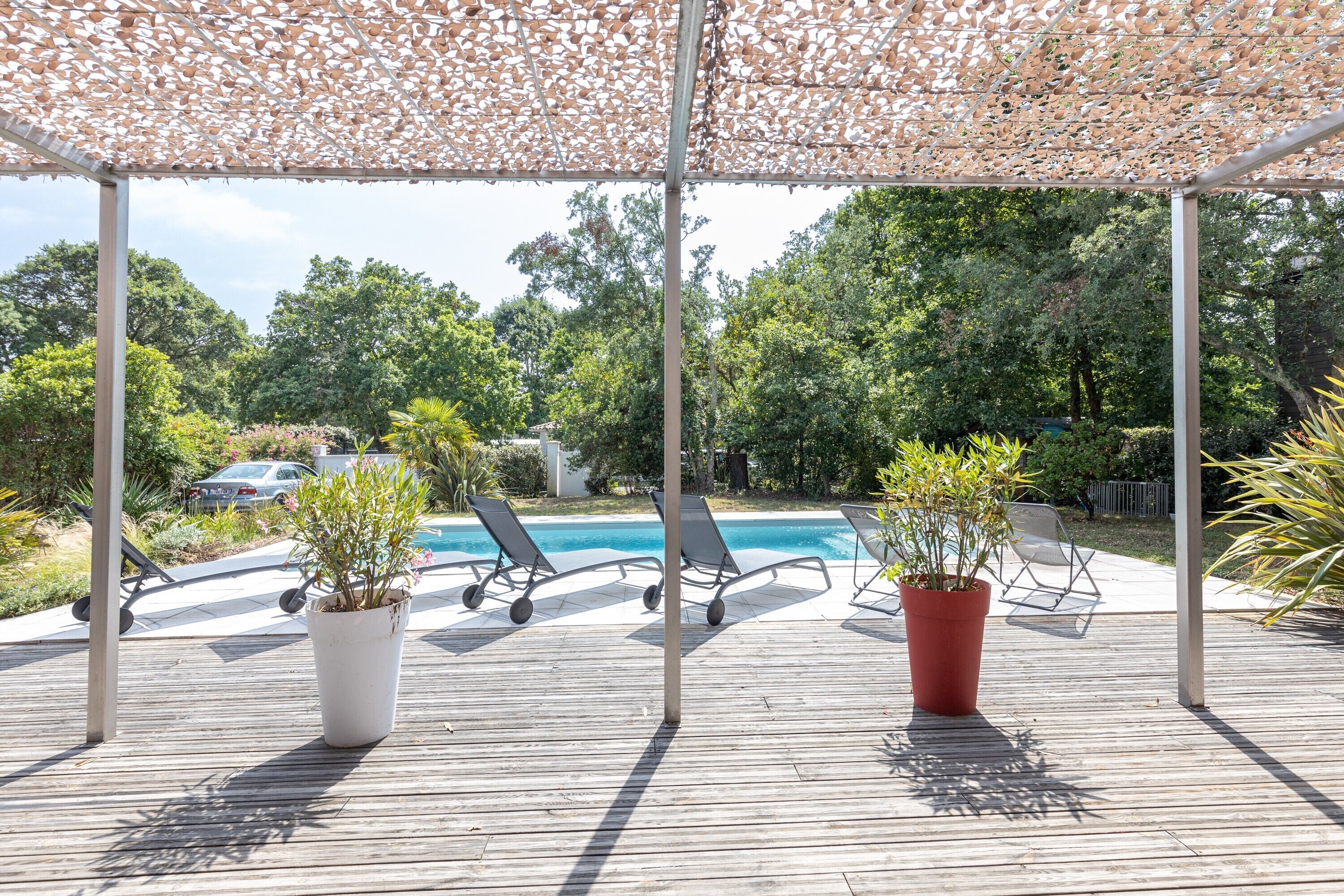 A wooden deck with a pool, lounge chairs, and potted plants.