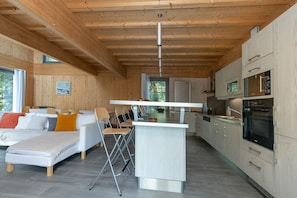 A modern interior with a sofa, dining table, chairs, kitchen area, and wooden ceiling.