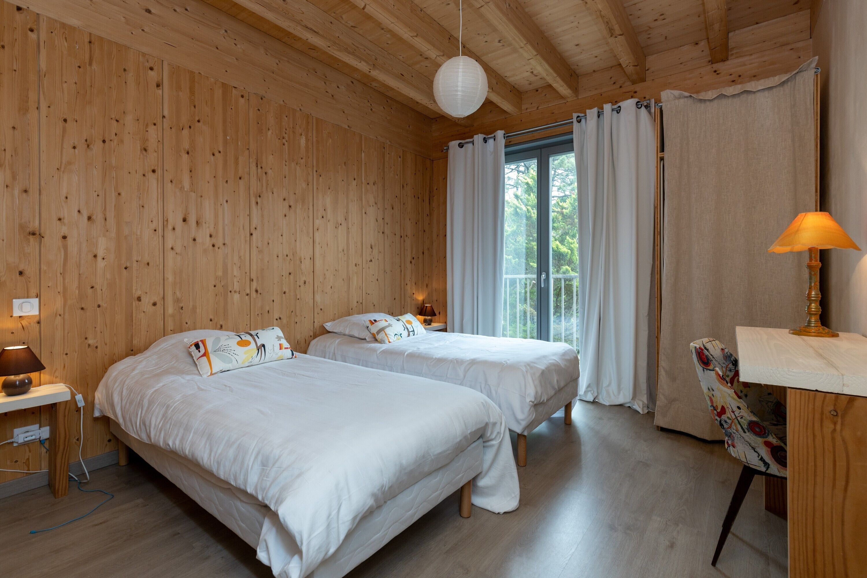 Una habitación con paneles de madera, dos camas, un escritorio con lámpara y una silla.