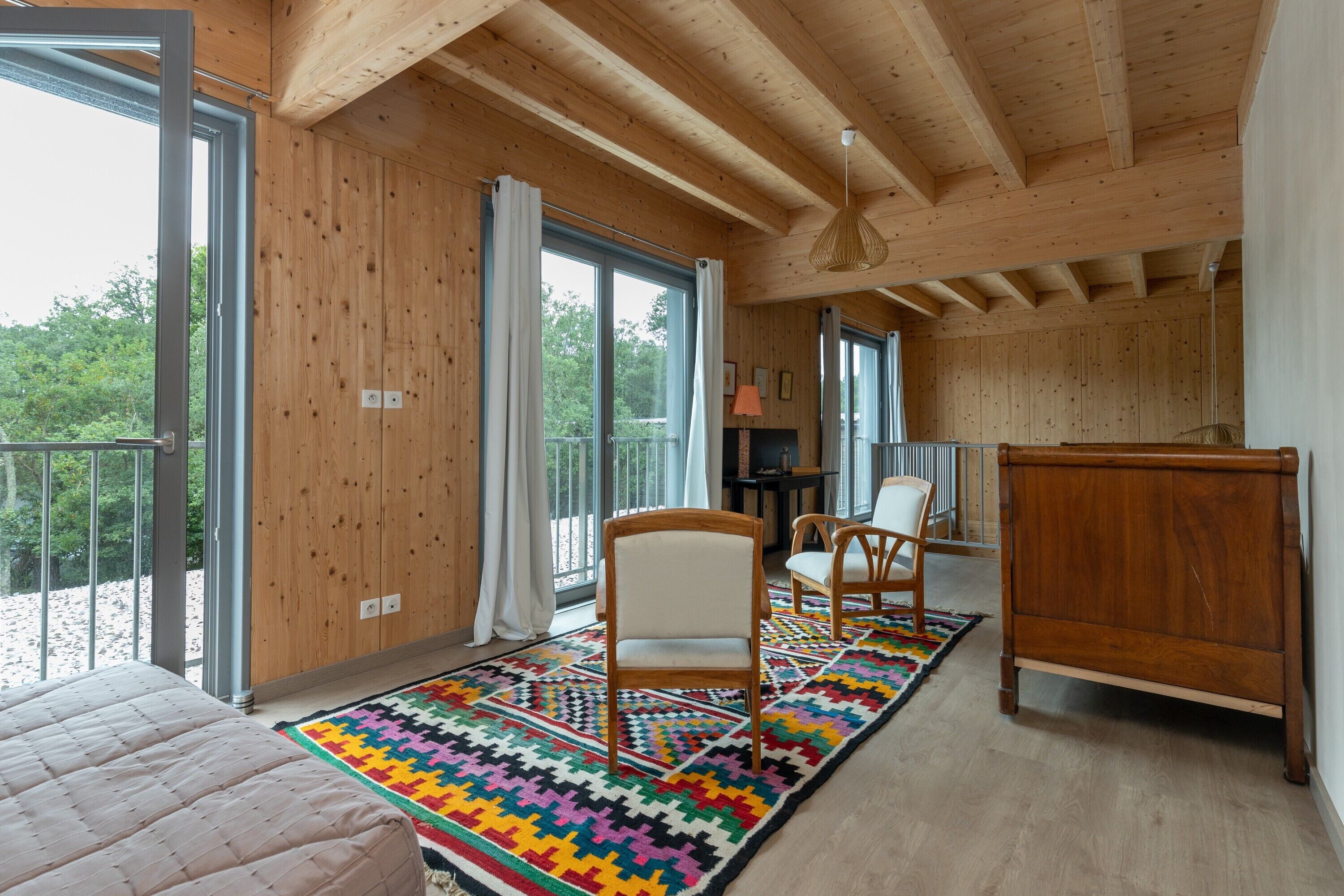 A room with a bed, a wooden desk, a chair, and a colorful rug.