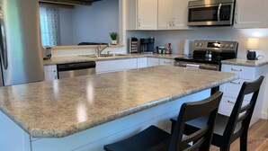 A modern kitchen with white cabinets, a granite countertop, stainless steel appliances, and a bar stool.