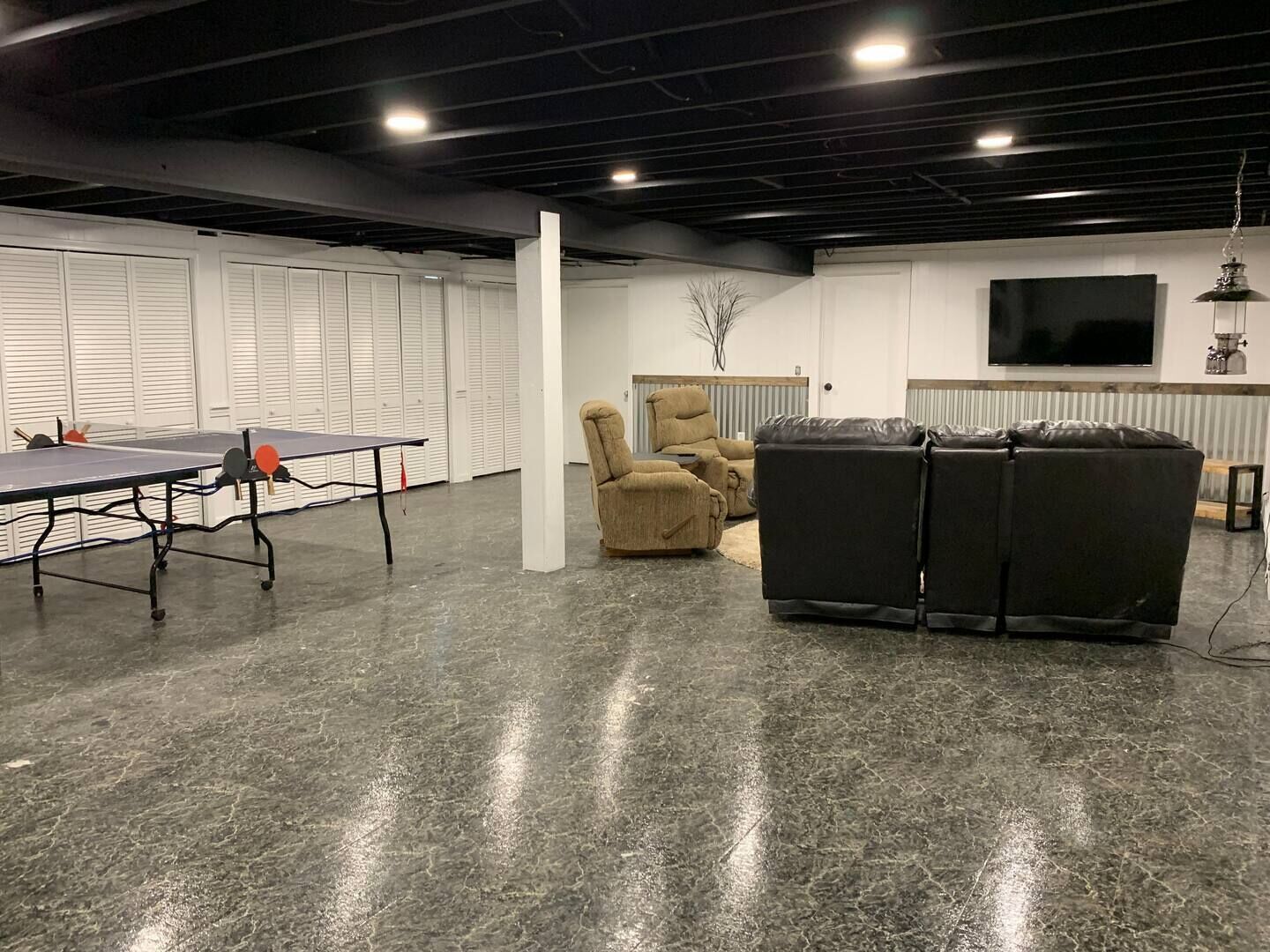 A spacious room with a ping pong table, a recliner, a sofa, and a TV on the wall.