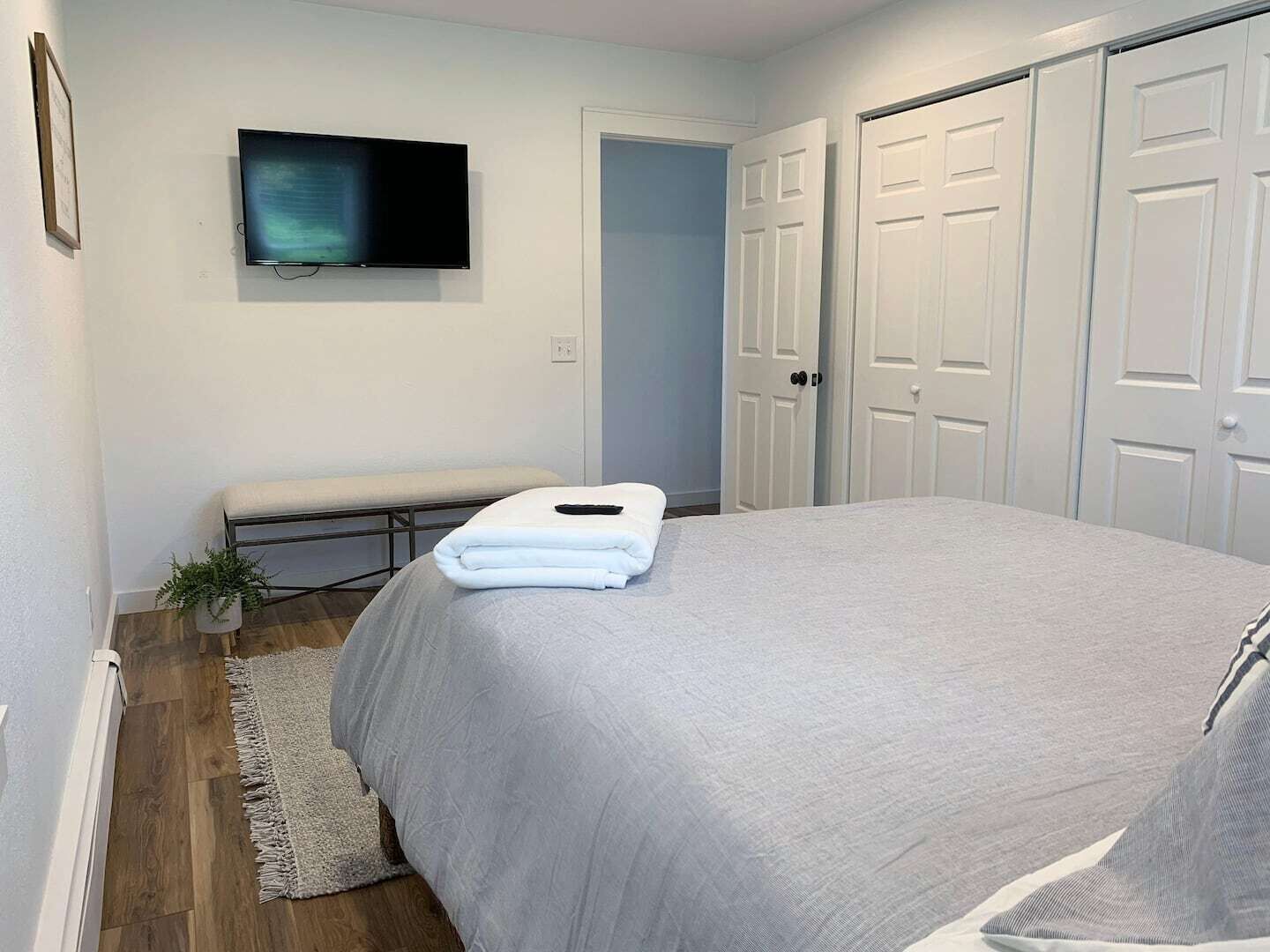 A bedroom with a bed, a bench, a TV, and a door.