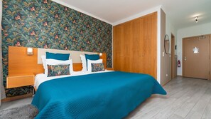 Quarto de hotel com cama, guarda-roupa de madeira e parede com padrão floral.