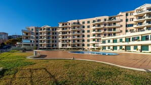 A multi-story residential building with balconies, a swimming pool, and a landscaped area.